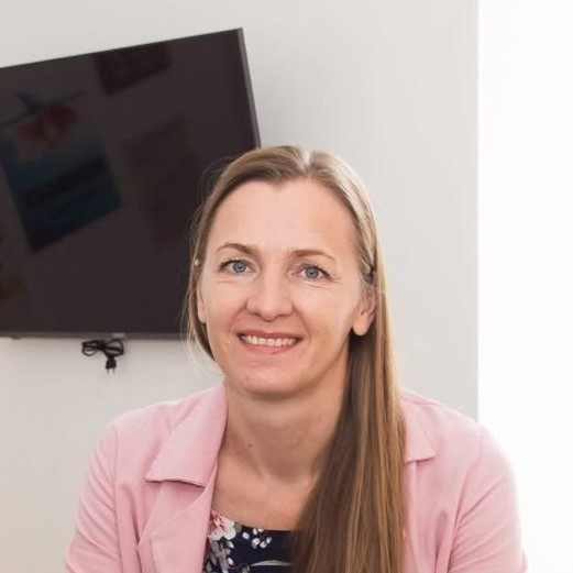 Nataliia Romanova Specjalista ds. administracji , młoda, uśmiechnięta kobieta w pomieszczeniu biurowym, w tle telewizor na ścianie