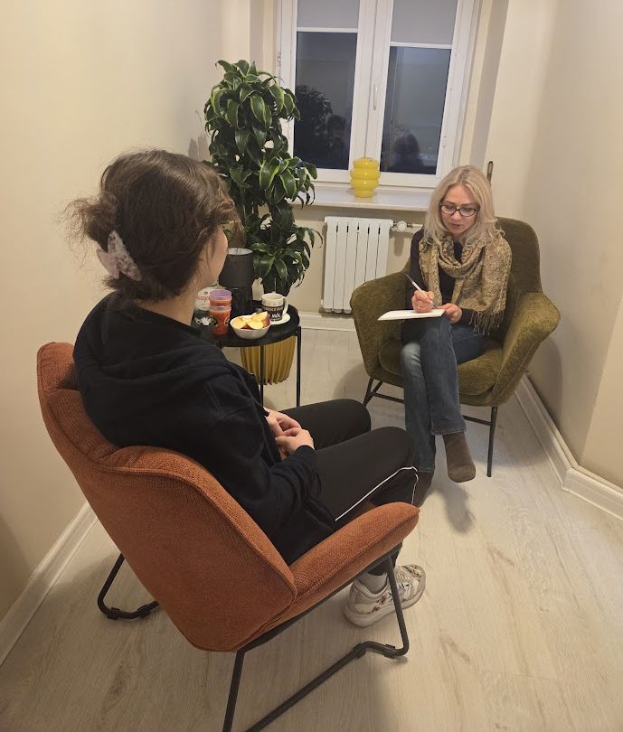 młoda dziewczyna rozmawia z psycholog robiącą notatki; siedzą w przytulnym pomieszczeniu z komfortowymi fotelami
