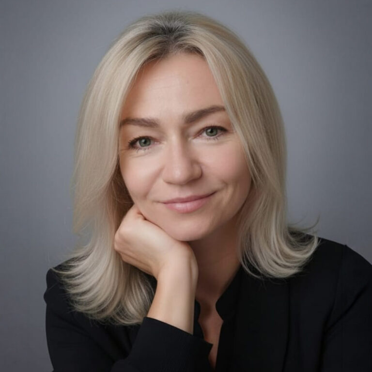 Anna Pochopień - pogodna, młoda kobieta z blond włosami do ramion, w czarnej marynarce, podpiera prawą dłonią podbródek; profesjonalny image