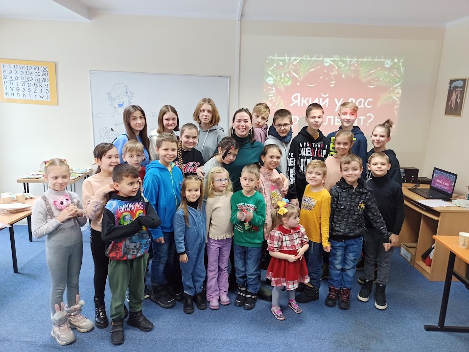 szeroko uśmiechnięta Sievil Abiieva stoi otoczona dziećmi w sali lekcyjnej