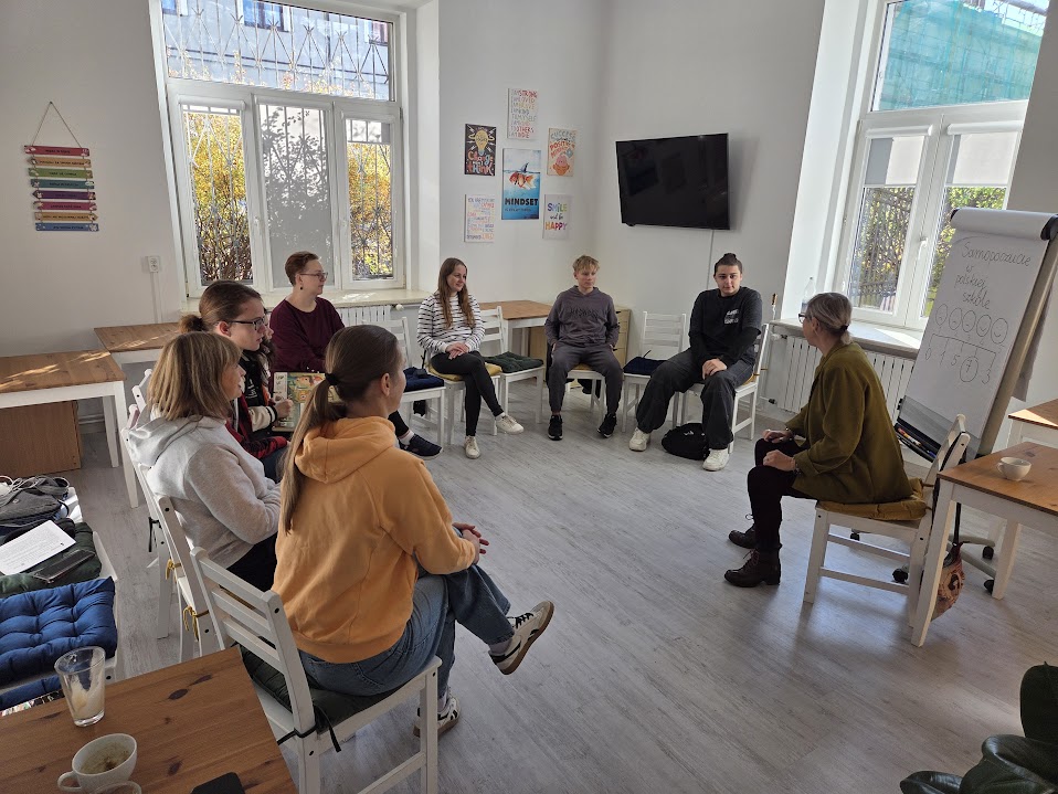 zajęcia językowe - grupa młodych ludzi z nauczycielką siedzi w okręgu w pomieszczeniu stowarzyszenia