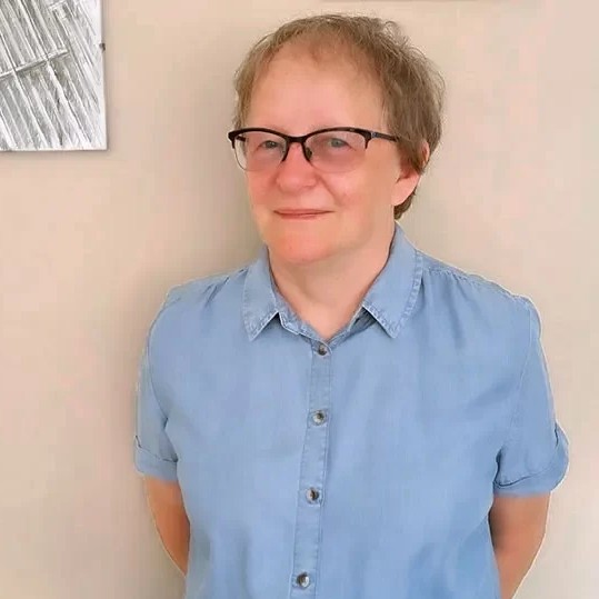 Barbara Brożyna - delikatnie uśmiechnięta kobieta w okularach i błękitnej koszuli