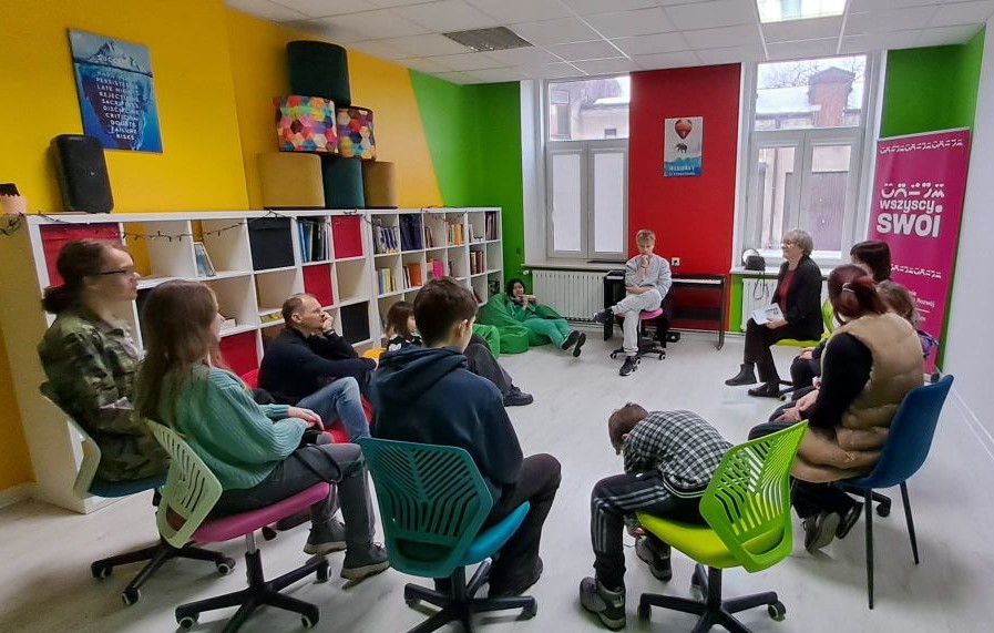 młodzież siedzi na krzesłach wokół nauczycielki w kolorowym pomieszczeniu Centrum Wszyscy Swoi