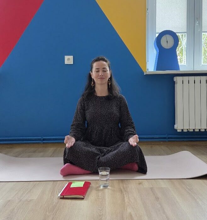Sievil Abbieva prowadzi medytację siedząc na macie w pozycji medytacyjnej i z zamkniętymi oczami
