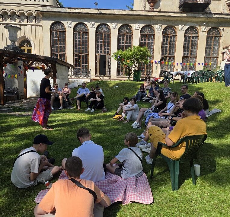 spotkanie młodzieży na trawniku dziedzińca Pałacyku Zielińskiego w Kielcach; w tle łukowate okna budynku