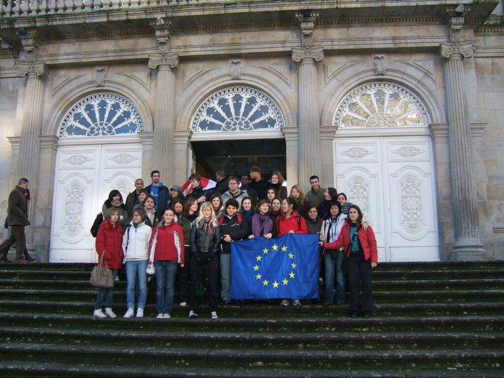grupa młodzieży z flagą unii europejskiej pozuje na schodach do zabytkowego budynku