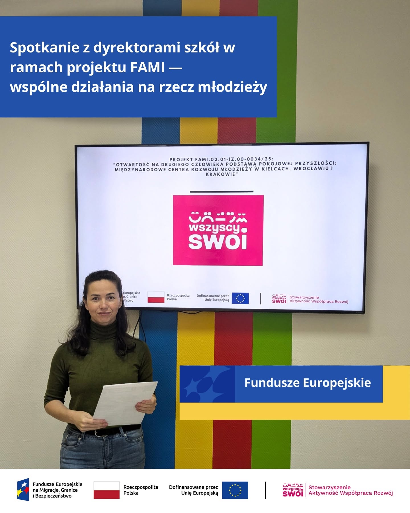 Kobieta stojąca w pomieszczeniu na tle ekranu z logo projektu Wszyscy Swoi oraz nagłówkiem o spotkaniu z dyrektorami szkół w ramach projektu FAMI.