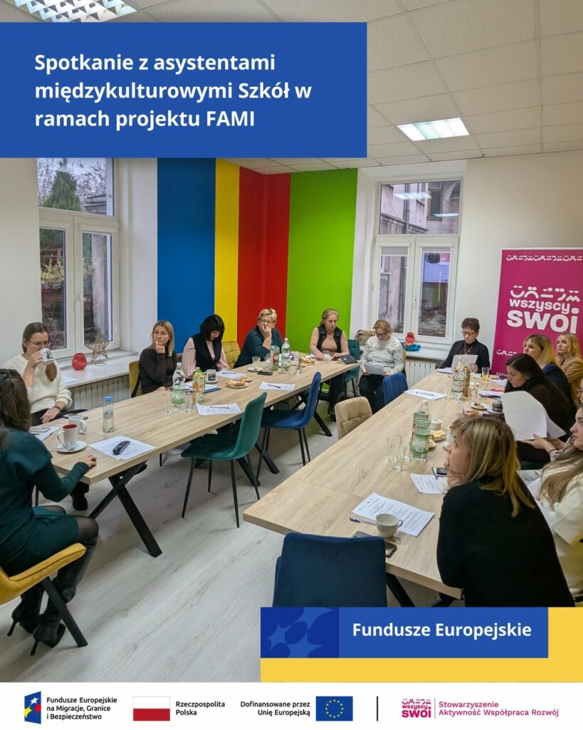 Spotkanie w sali szkoleniowej z asystentami międzykulturowymi zgromadzonymi wokół stołów usytuowanych w kształcie litery U.